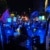 Durch eine Lücke zwischen zwei Polizeiautos durch fotografiert ist eine größere Menschenmenge zu sehen, die vor einer Polizeikette steht. Einige Personen schwenken Fahnen oder tragen Schilder, sie werden von Blaulicht angestrahlt.