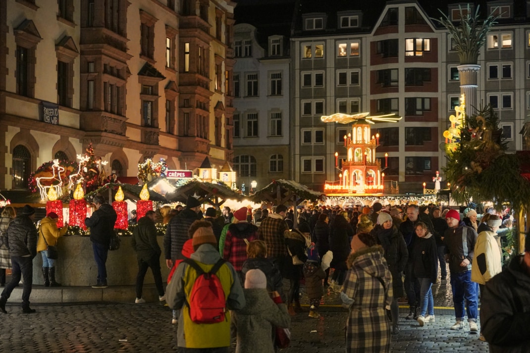 Auf dem Leipziger Nikolaikirchhof stehen mehrere Weihnachtsmarkt-Buden und eine Weihnachtspyramide. Dazwischen sind dutzende Personen beim gemütlichen Schlendern zu sehen.