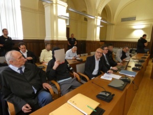 Anklagebank, Angeklagte, Dolmetscher und Verteidiger sitzend im Gerichtssaal.