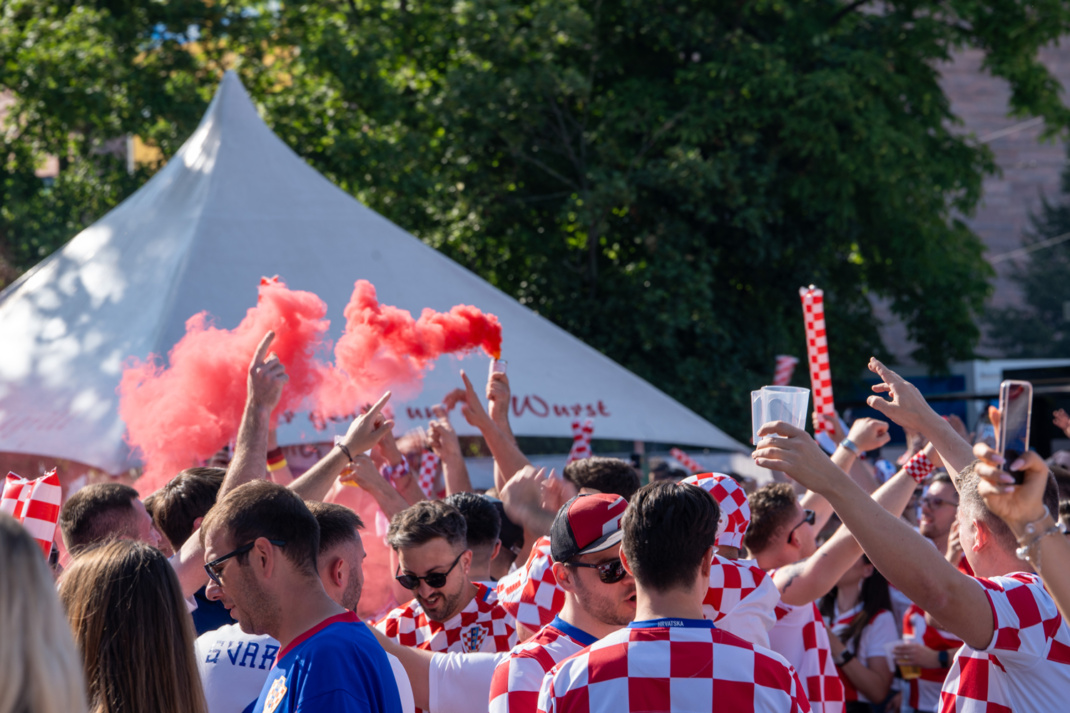 Kroatische Fußball-Fans beim Fanmarsch am 24. Juni 2024 in Leipzig, zu sehen sind Rauchfackeln und Plastikbecher, die in die Höhe gereckt werden.