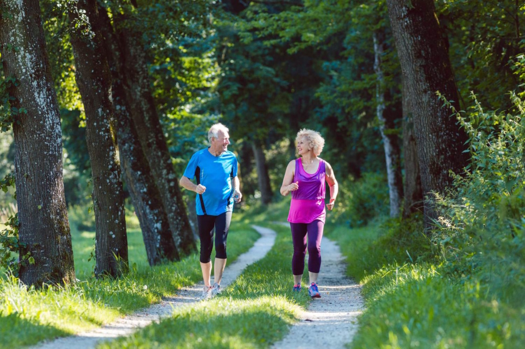 Zwei ältere Personen joggen durch einen Wald.