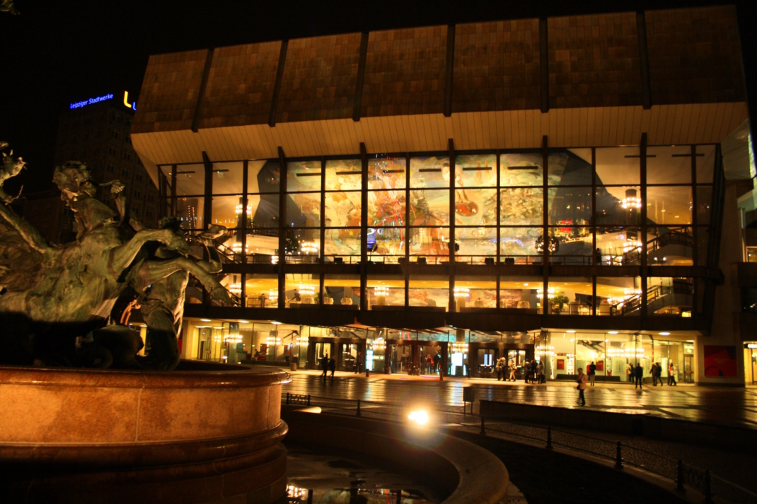 Beleuchtetes Gewandhaus mit Mendebrunnen in der Dunkelheit.