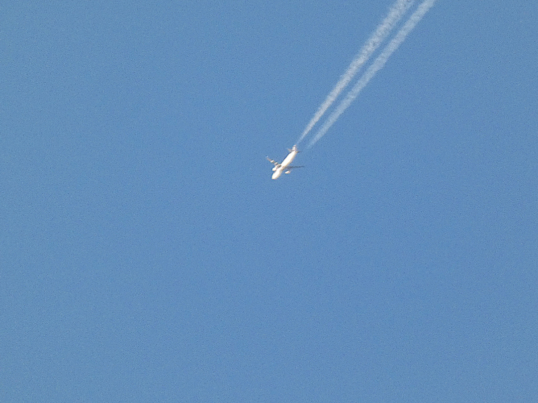 Flugzeug mit Kondensstreifen am blauen Himmel.