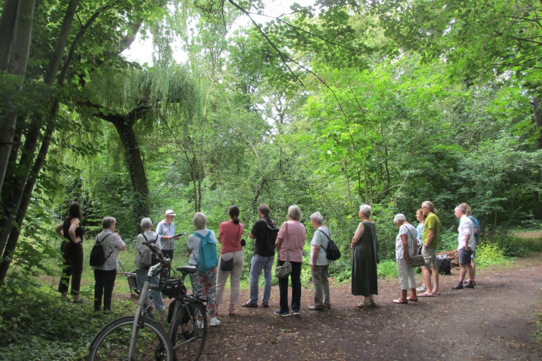 Menschen stehen im Wald und hören einer Lesung zu