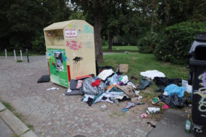 Altkleidercontainer, umgeben von Textilien und Müllsäcken.