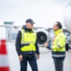 Zwei Männer in grellen Arbeitsjacken sprechen miteinander, im Hintergrund ist ein stehendes Flugzeug erkennbar.