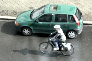 Radfahrer neben grünem Auto.