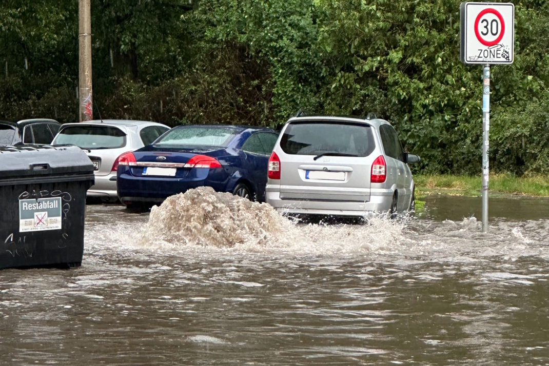 Überschwemmung mit Regenwasser, parkende PKW, Mülltonne.