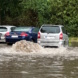 Überschwemmung mit Regenwasser, parkende PKW, Mülltonne.