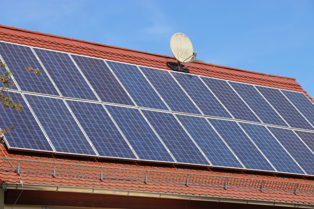 Dach mit Satellitenschüssel und Solaranlage, blauer Himmel