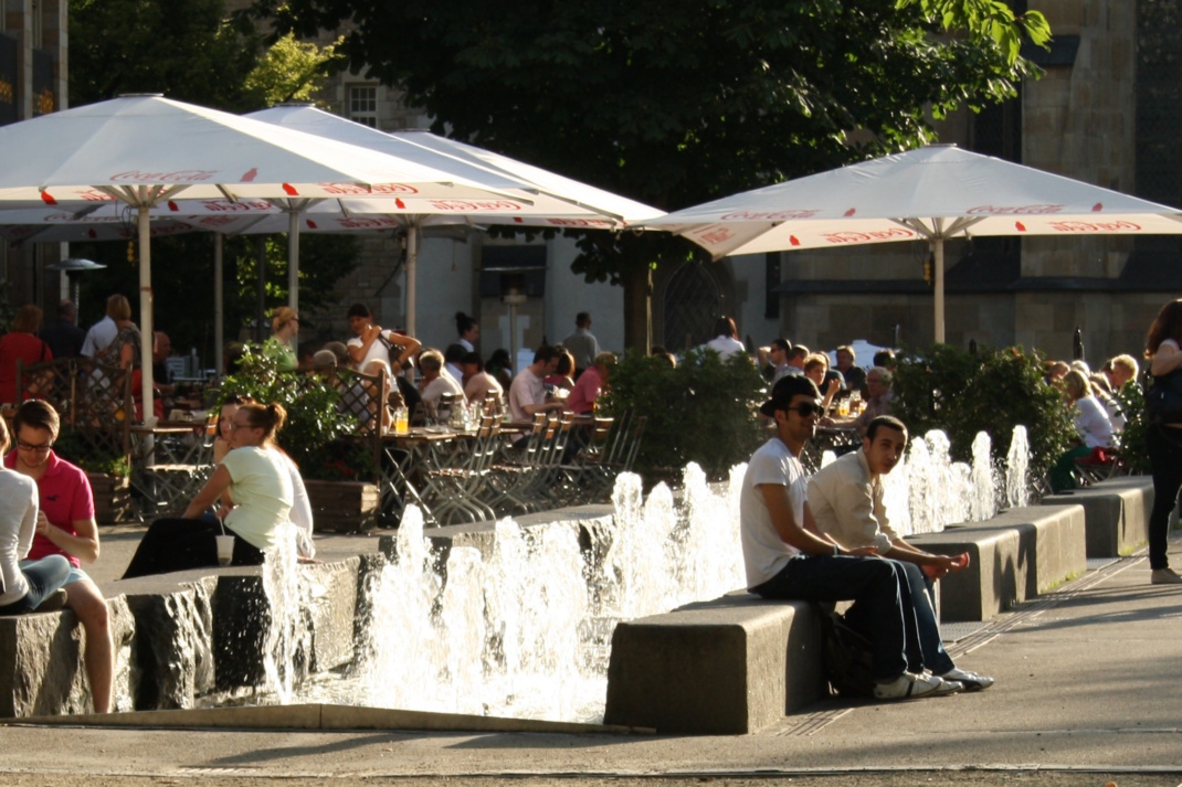 Menschen im Freisitz unter Sonnenschirmen.