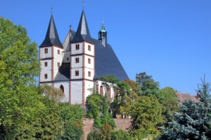 Helle Kirche mit zwei Türmen, Bäume und blauer Himmel.