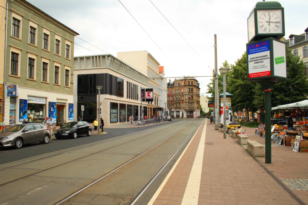 Städtischer Platz mit Wohnhäusern, Straßenbahnschienen und Autos.