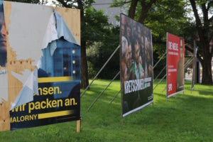 Große Wahlplakate, eines davon angerissen.