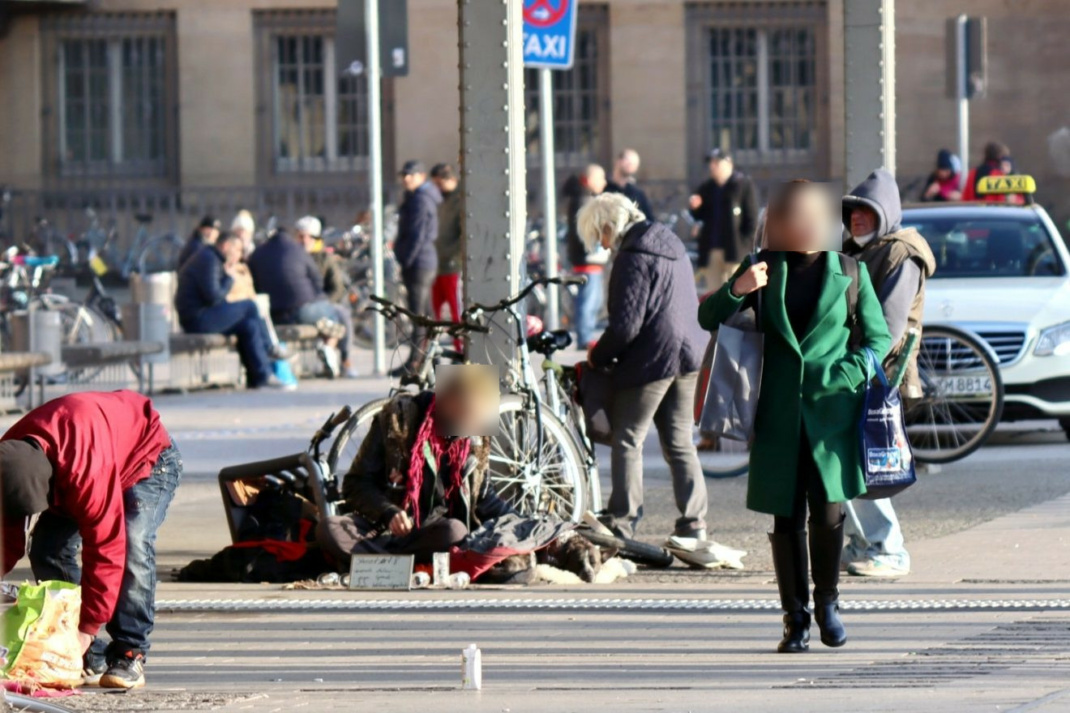 Obdachlose Personen auf Bahnhofsvorplatz, viele Menschen unterwegs,