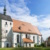 Helle Kirche mit rotem Dach und umgeben von Bäumen, blauer Himmel.