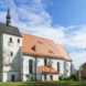 Helle Kirche mit rotem Dach und umgeben von Bäumen, blauer Himmel.