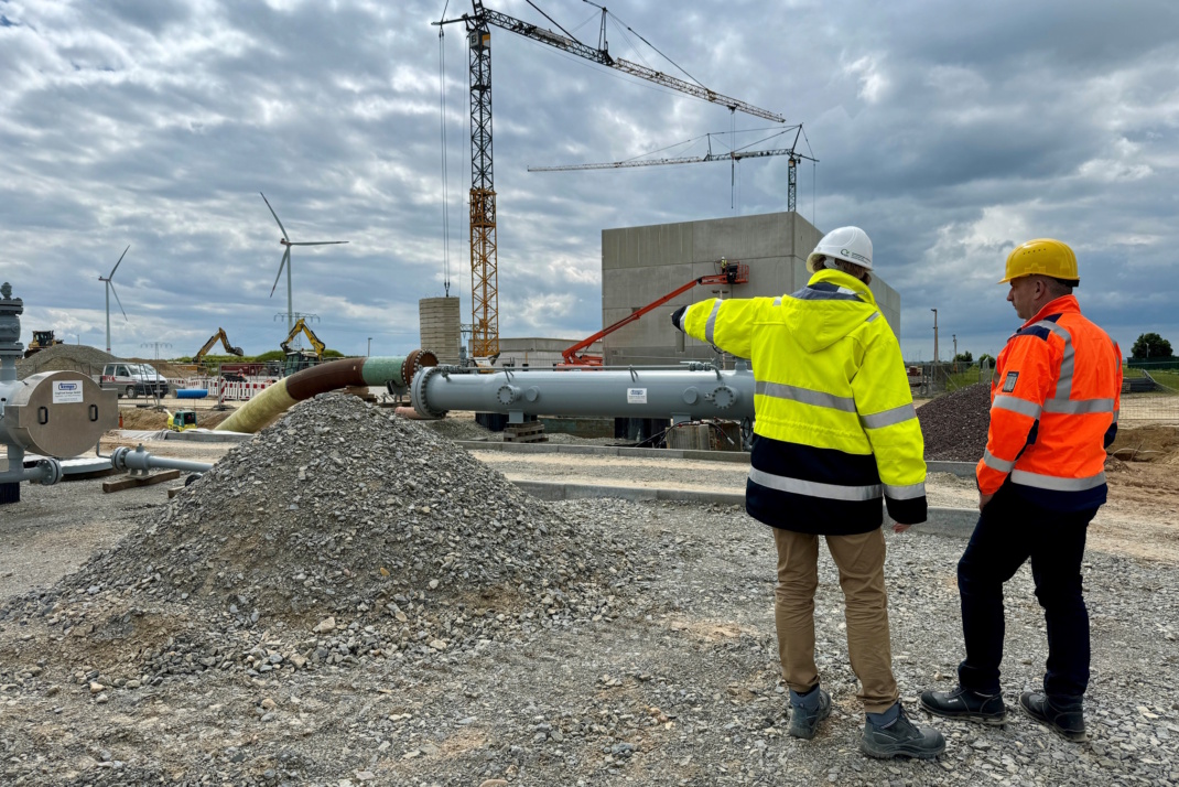 Baustelle mit Kran und Gasleitung, zwei Personen mit Warnjacken und Helmen.