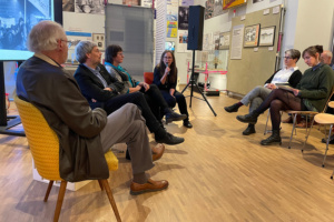 Vier Menschen in Stühlen auf einem Podium, davor Publikum