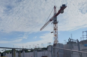 Baustelle mit Kran, der sich gegen blauen Himmel und Wolken abzeichnet.