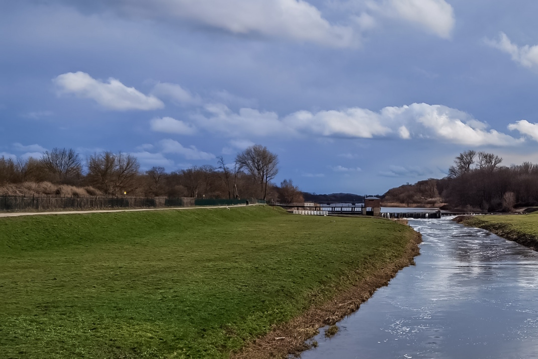 Flusslandschaft mit Weg, grüner Hang, blauer Himmel und Wolken,