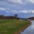 Flusslandschaft mit Weg, grüner Hang, blauer Himmel und Wolken,