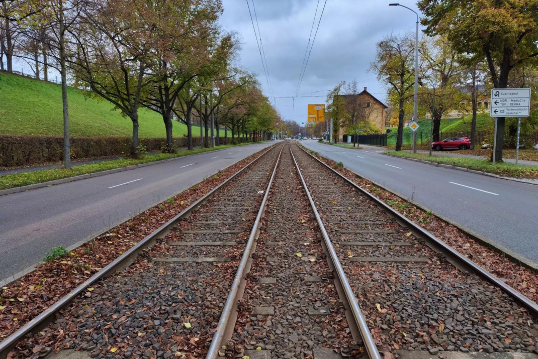 Straßenbahntrasse in der Mitte der Fahrbahn, zweigleisig, daneben die asphaltierten Fahrspuren, Gehweg und Bäume.