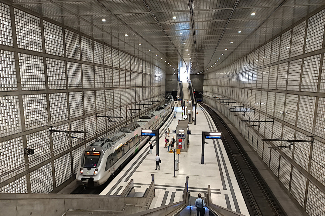 Rolltreppe, Blick auf Bahnsteig mit Menschen und Zug in S-Bahn-Station.