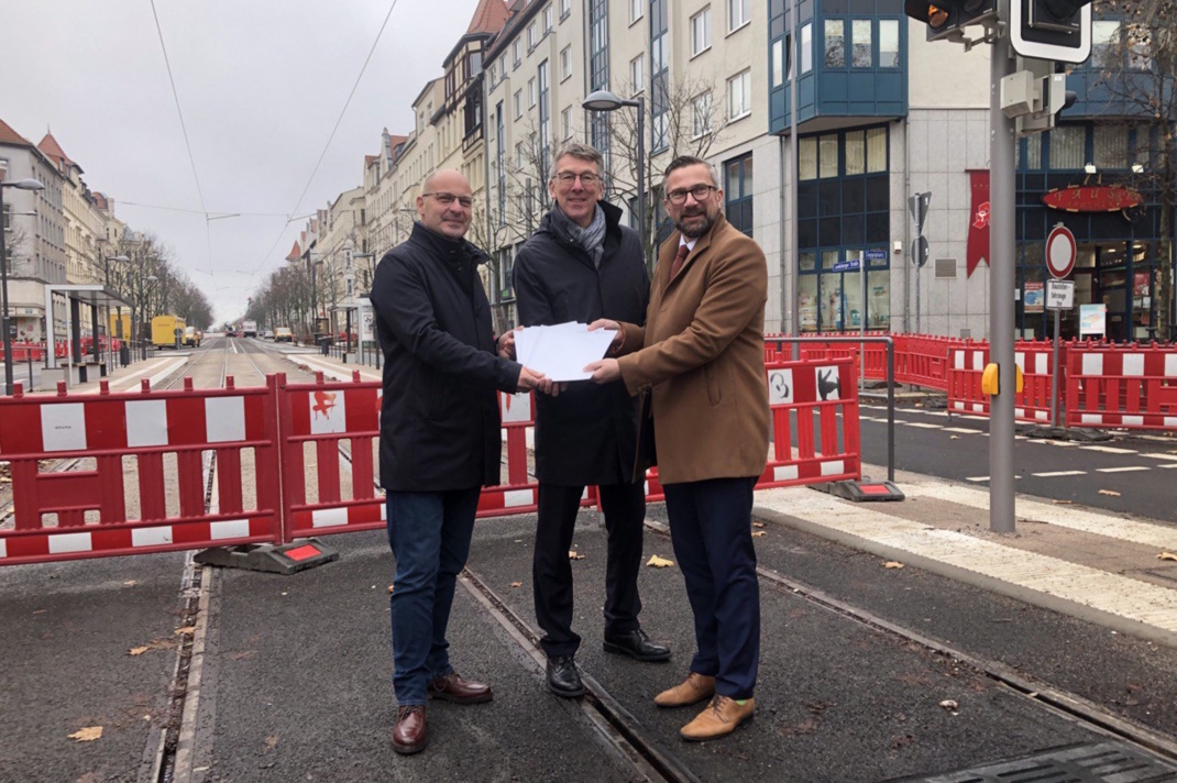 Übergabe der Fördermittelbescheide in der Landsberger Straße mit Stefan Röll (Bereichsleiter Infrastruktur der LVB), Ulf Middelberg (Sprecher der Geschäftsführung der LVB) und Wirtschaftsminister Martin Dulig. Die drei Personen stehen nebeneinander und halten den Bescheid.