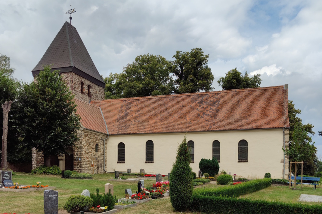 Helles Kirchengebäude mit Friedhof.