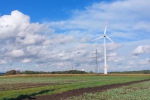 Windkraftanlage auf freiem Feld, blauer Himmel und Wolken.