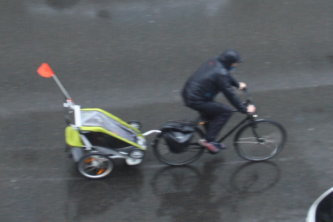 Radfahrer mit Kinderanhänger im Regen.