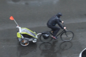 Radfahrer mit Kinderanhänger im Regen.