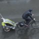 Radfahrer mit Kinderanhänger im Regen.