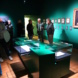 Ausstellungseröffnung, Personen stehen in halbdunklem Museumsraum.